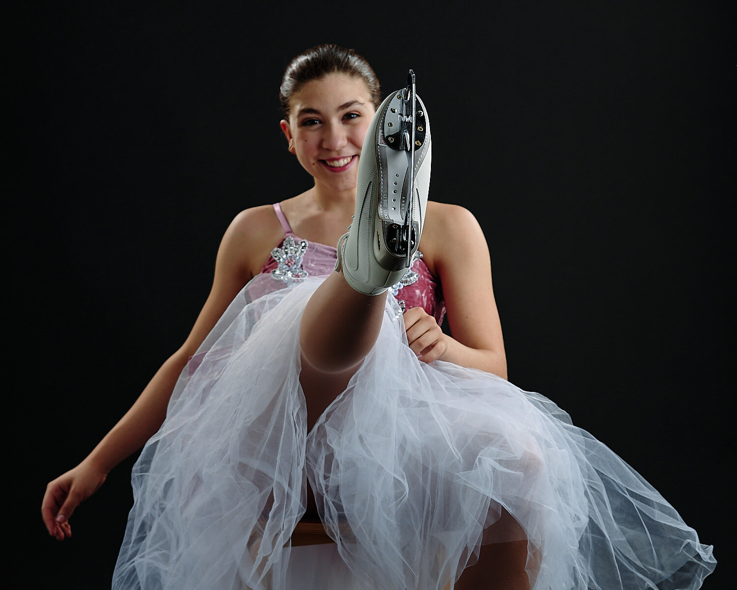  Ella Sanfilippo is posing in her ice skating costumes and made in Italy white skates in a professional photography studio against a black background. She has an athletic body and a beautiful face. 