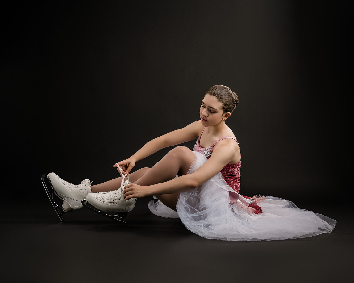  Ella Sanfilippo is posing in her ice skating costumes and made in Italy white skates in a professional photography studio against a black background. She has an athletic body and a beautiful face. 