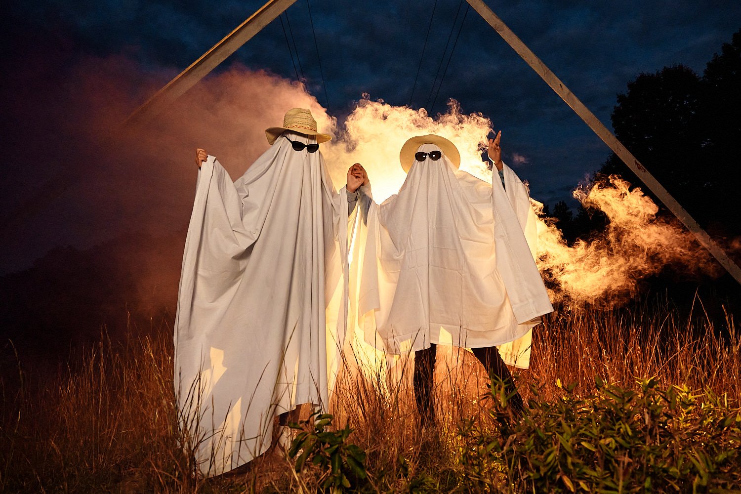  Alena Gurevich and her friend Aekam Kaur are dressed as ghosts for Halloween in October 2020. They wear sunglasses and there’s orange and purple smoke around them in the field. 