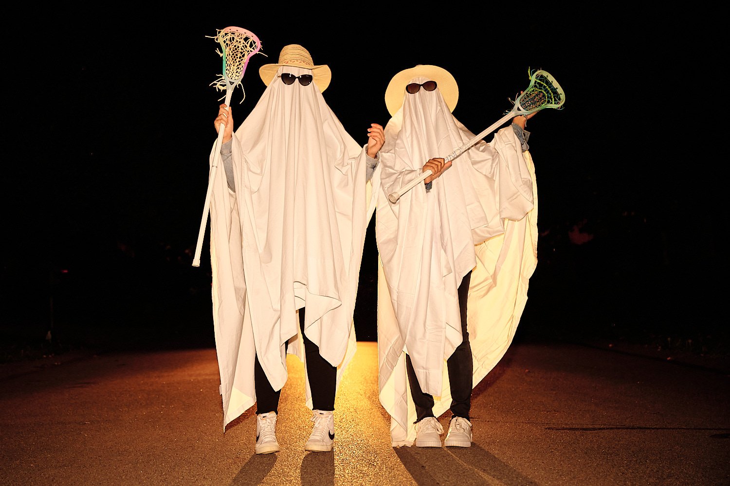  Alena Gurevich and her friend Aekam Kaur are dressed as ghosts for Halloween in October 2020. They wear sunglasses and there’s orange and purple smoke around them in the field. 