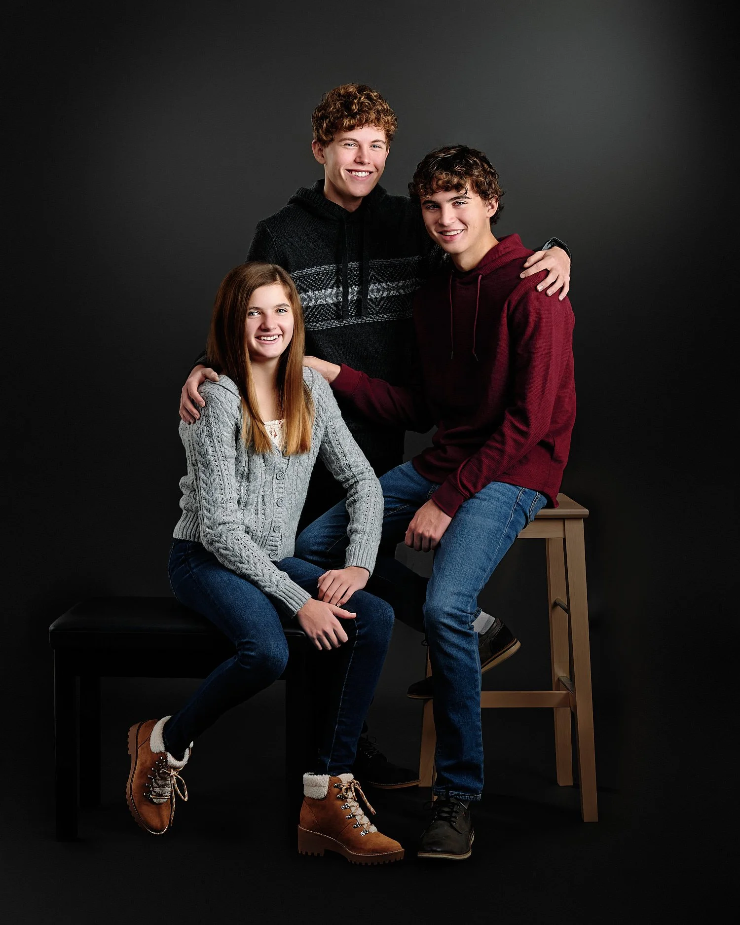  Ryan, Mason and Keira Scott are posing for their family portraits in the studio with black background. They look beautiful with blond curly hair and grey eyes, dressed in cozy winter sweaters. 