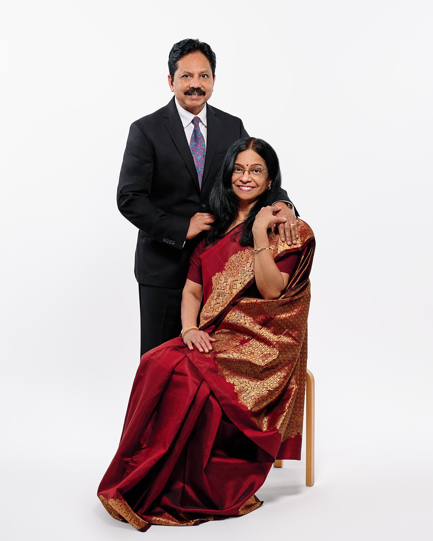  Mohandas Parappath and his wife Kanthi Menon are posing for family portraits with their daughters Kamya and Maya in a photography studio. Their bright colorful dresses pop out against white background 