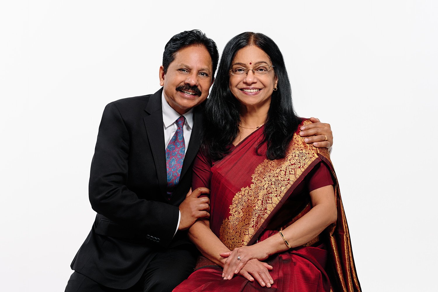  Mohandas Parappath and his wife Kanthi Menon are posing for family portraits with their daughters Kamya and Maya in a photography studio. Their bright colorful dresses pop out against white background 