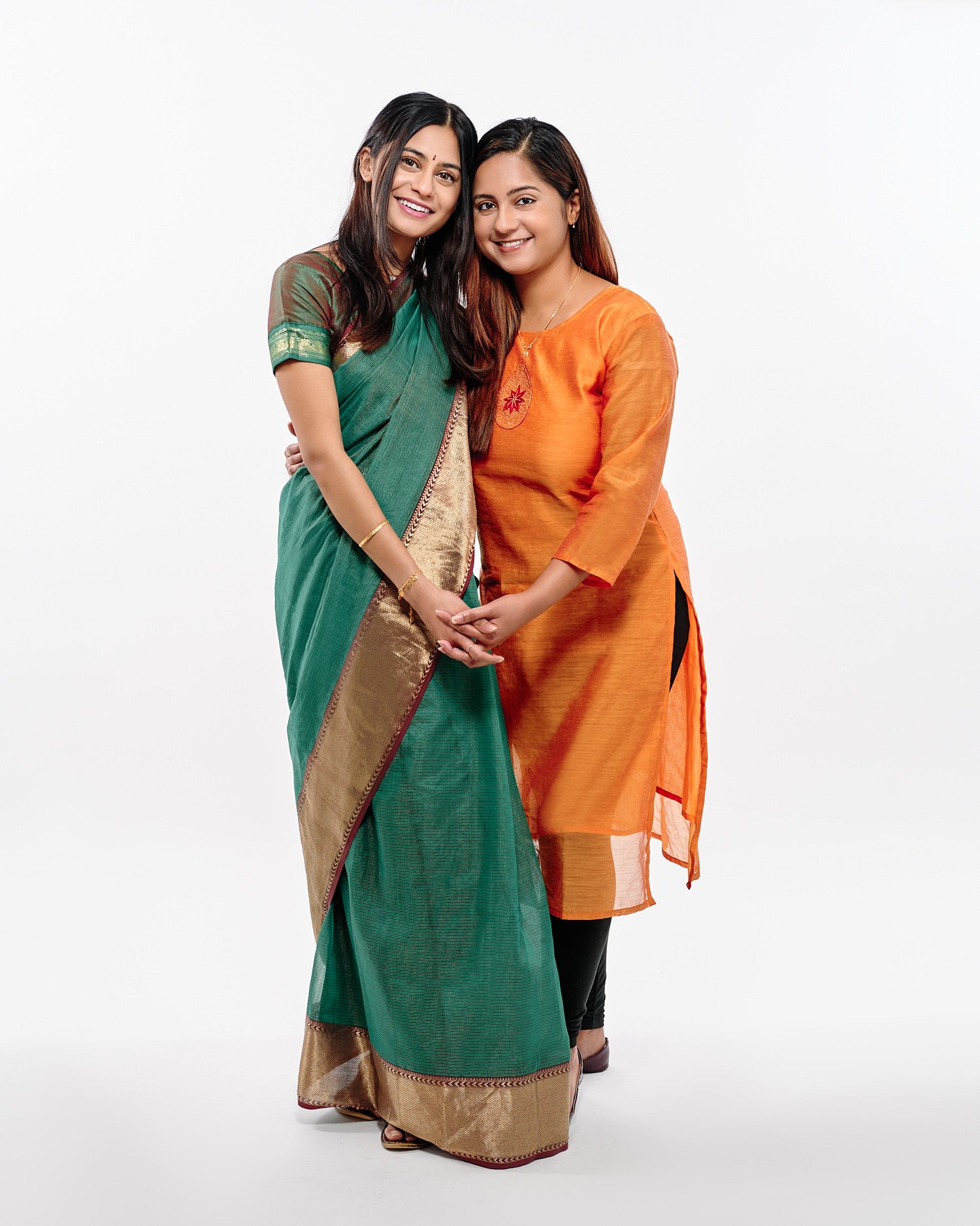  Mohandas Parappath and his wife Kanthi Menon are posing for family portraits with their daughters Kamya and Maya in a photography studio. Their bright colorful dresses pop out against white background 