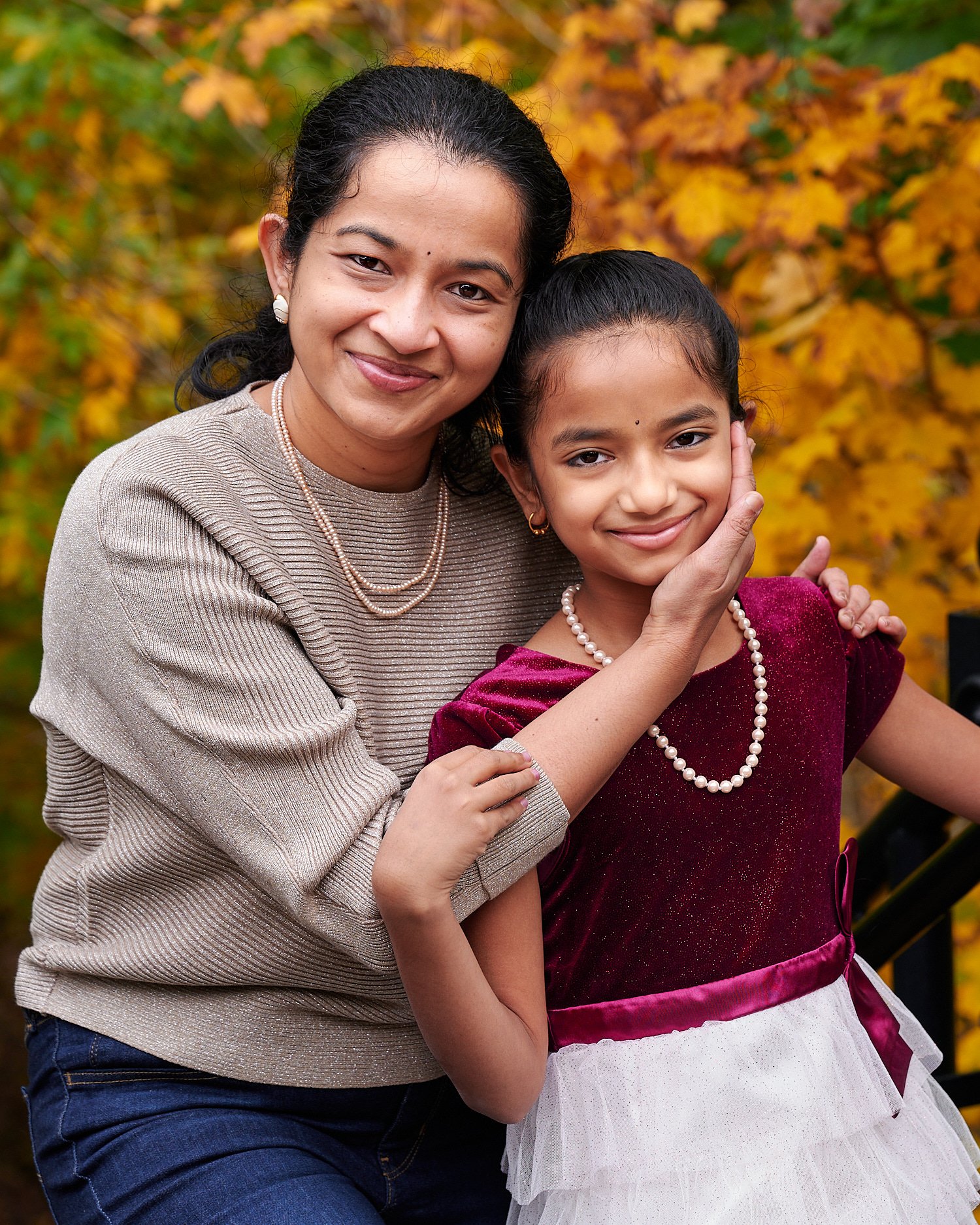  Mother  is posing with her pre-teen daughter in front of Phipps Conservatory and Botanical Gardens of Pittsburgh, Pennsylvania. The girl is wearing a burgundy ball dress and pearls. 