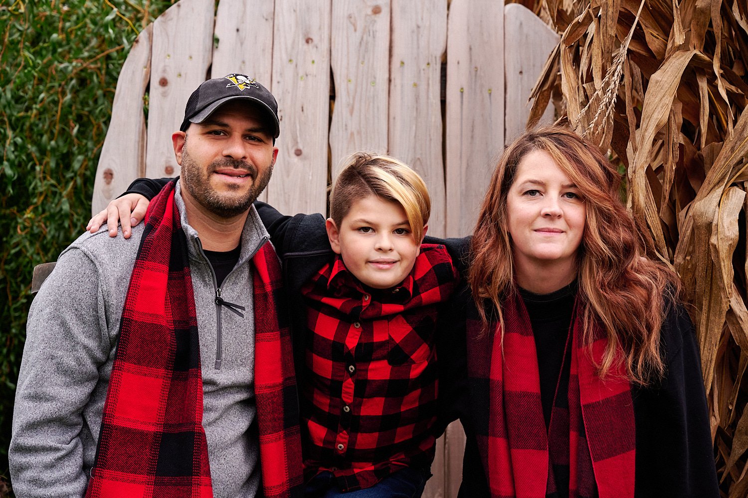  Andrea D’Alessandro is posing with her extended family in front of Phipps Conservatory and Botanical Gardens of Pittsburgh, PA. The large group is wearing red checked flannel shirts and blue jeans. 