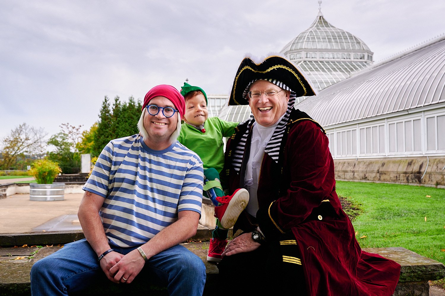  Michaela Robbins is posing with her husband, son and parents in front of Phipps Conservatory and Botanical Gardens of Pittsburgh, PA. The family is dressed in Peter Pan costumes - Tinker Bell, Pirate. 