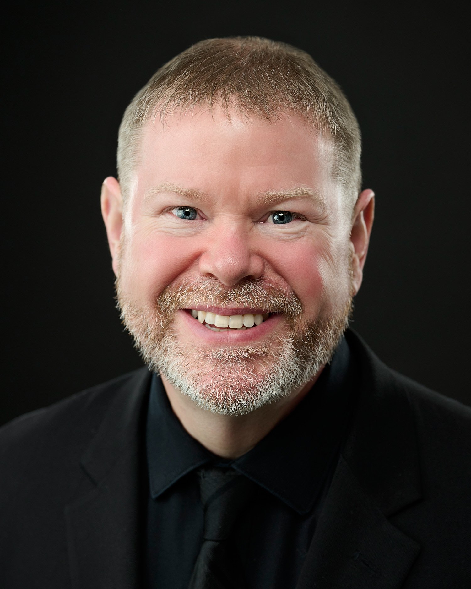  Tim Heavner is posing for his business headshots in a professional photography studio with a dark black background. Timothy is a pianist and is portrayed with his keyboard full length and close-up. 