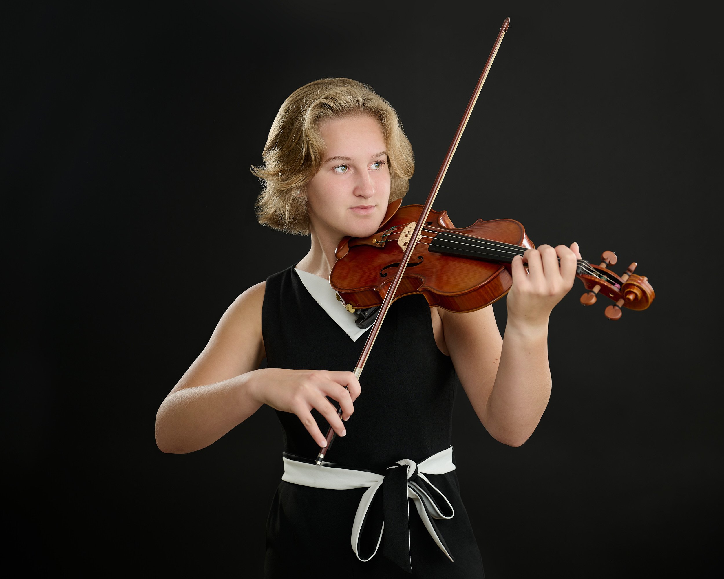  HOUSTON, TEXAS - JUNE 15TH 2022: a beautiful 16-year-old girl with fair skin and short blond hair is posing for studio portraits with her violin made by the string instruments maker Phillip Injeian. 
