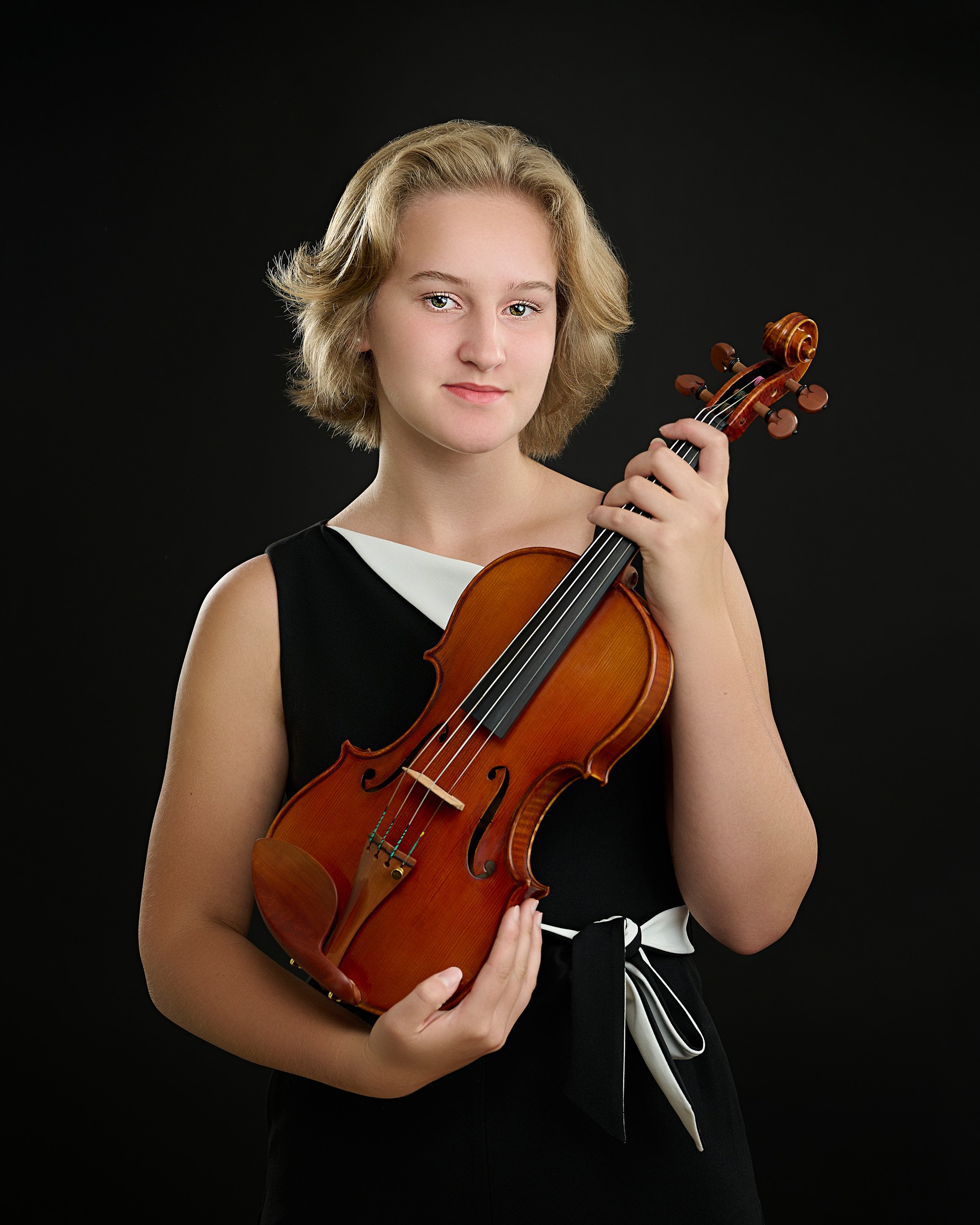  HOUSTON, TEXAS - JUNE 15TH 2022: a beautiful 16-year-old girl with fair skin and short blond hair is posing for studio portraits with her violin made by the string instruments maker Phillip Injeian. 
