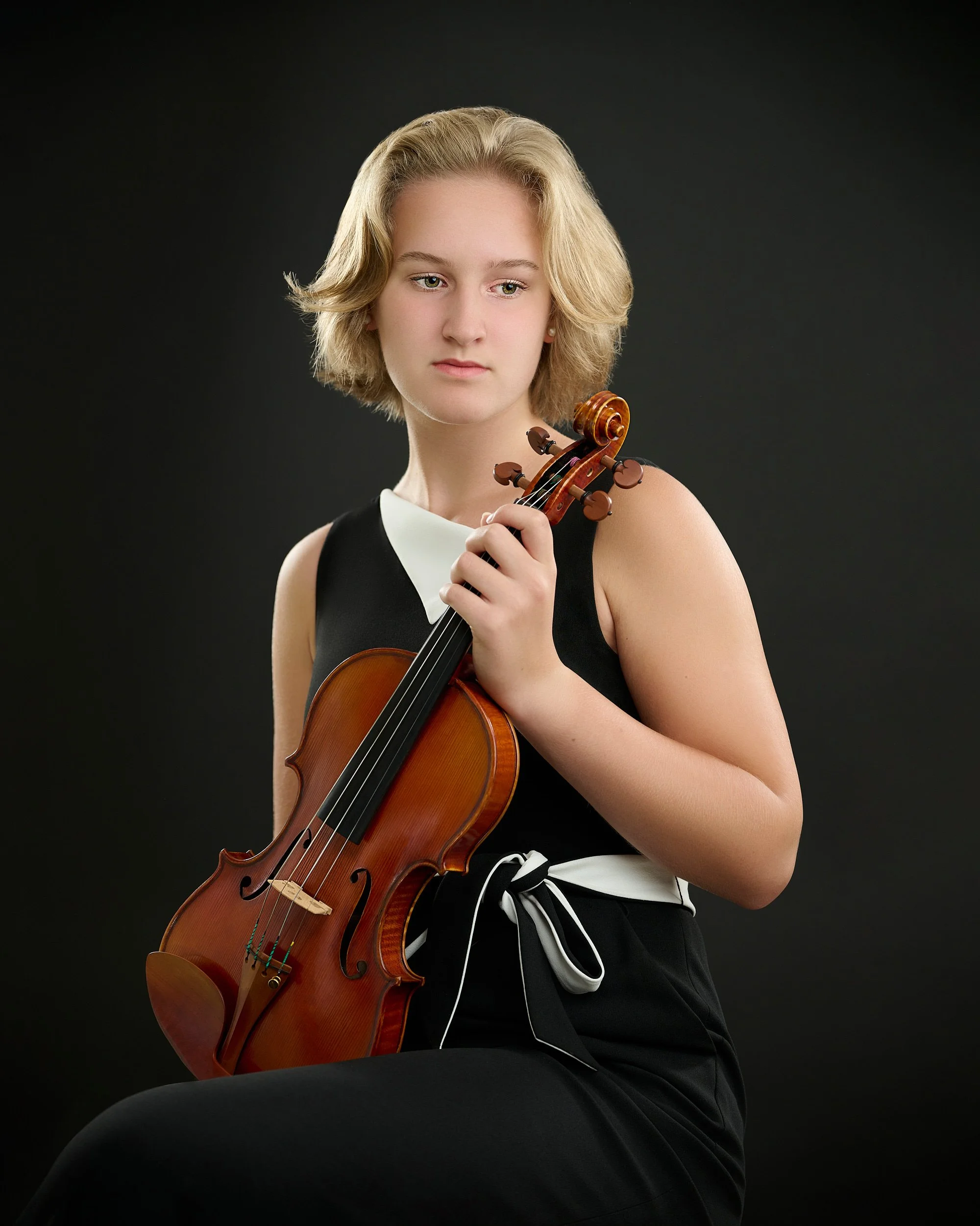 HOUSTON, TEXAS - JUNE 15TH 2022: a beautiful 16-year-old girl with fair skin and short blond hair is posing for studio portraits with her violin made by the string instruments maker Phillip Injeian.