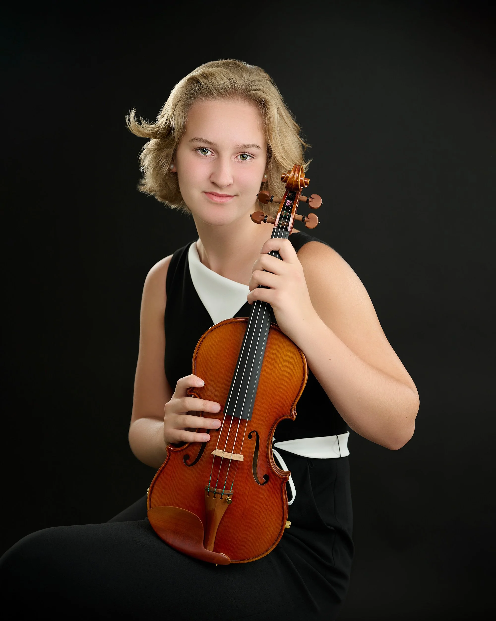 HOUSTON, TEXAS - JUNE 15TH 2022: a beautiful 16-year-old girl with fair skin and short blond hair is posing for studio portraits with her violin made by the string instruments maker Phillip Injeian. 