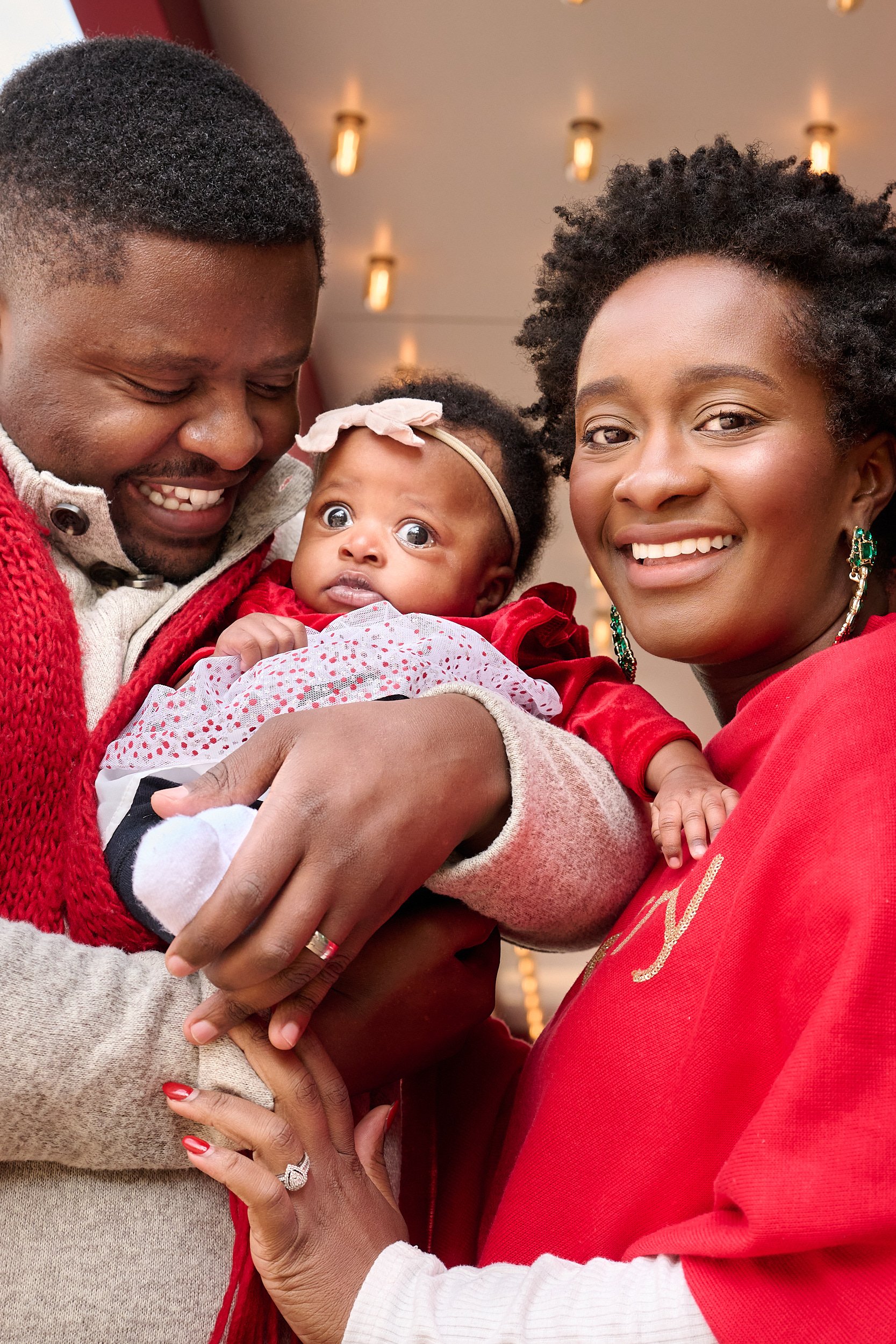  THE WOODLANDS, TEXAS - DECEMBER 2022: Deionfia Neza is posing for Christmas card portraits with her newborn daughter and her husband. The infant and her young parents are dressed in red and look happ 
