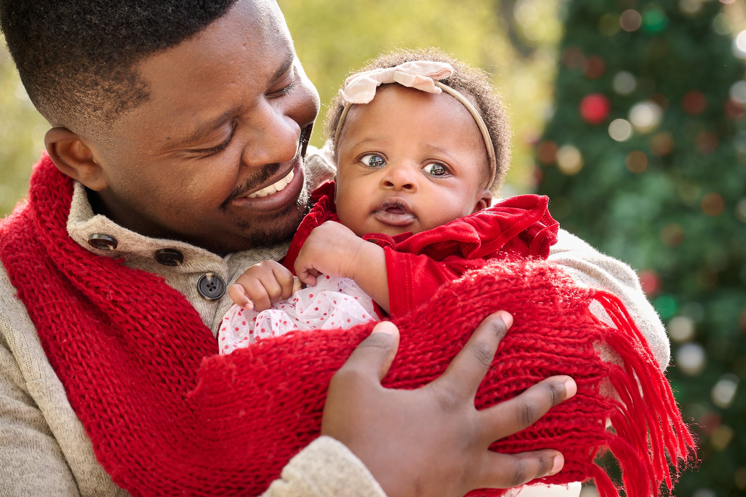  THE WOODLANDS, TEXAS - DECEMBER 2022: Deionfia Neza is posing for Christmas card portraits with her newborn daughter and her husband. The infant and her young parents are dressed in red and look happ 