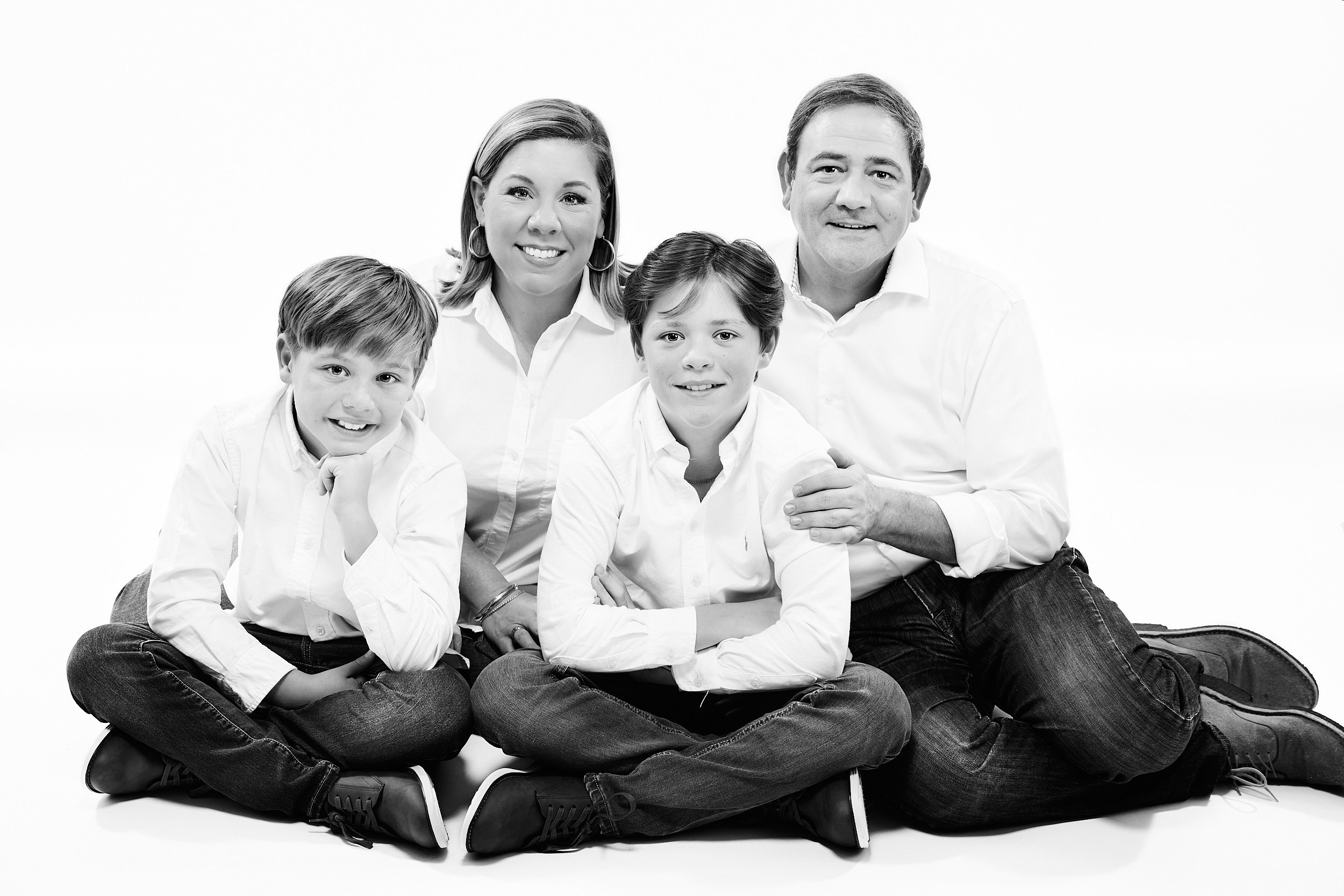  THE WOODLANDS, TEXAS - DECEMBER 2022: Emily Braud is posing for high key black and white portraits with her husband and two sons. They wear white shirts and blue jeans and look happy and healthy. 