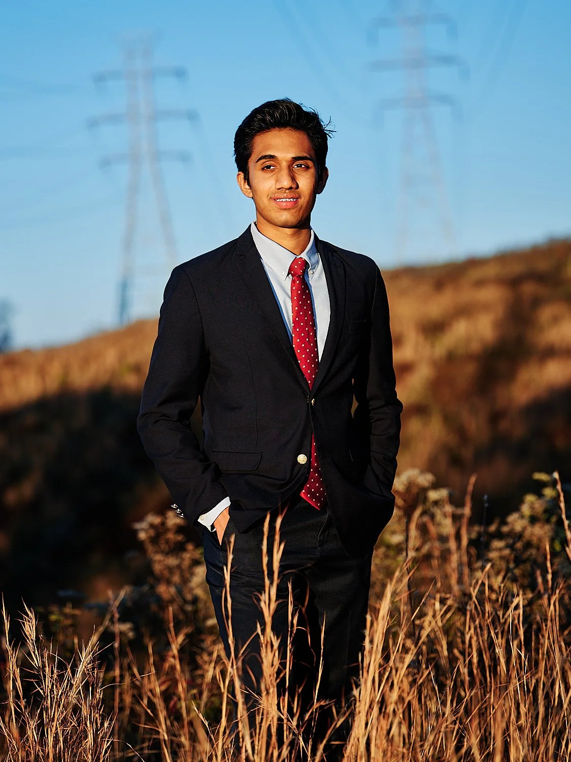  THE WOODLANDS, TEXAS - APRIL 2023: a handsome 17-year-old guy in a blue suit and red tie is posing for high school senior portraits for yearbook and wall art. He has shiny black hair and brown eyes. 