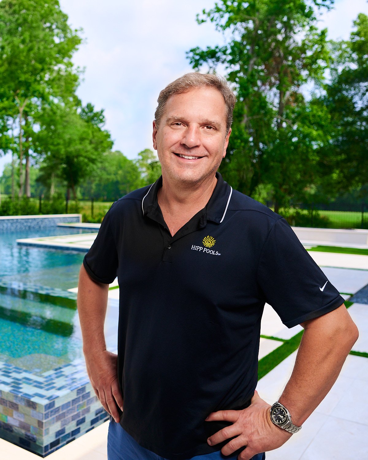  THE WOODLANDS, TEXAS - MAY 5th 2023: a pool guy is posing in front of an outdoor pool and spa with water features on a hot sunny day. The blue water is sparkling against the Mediterranean house. 