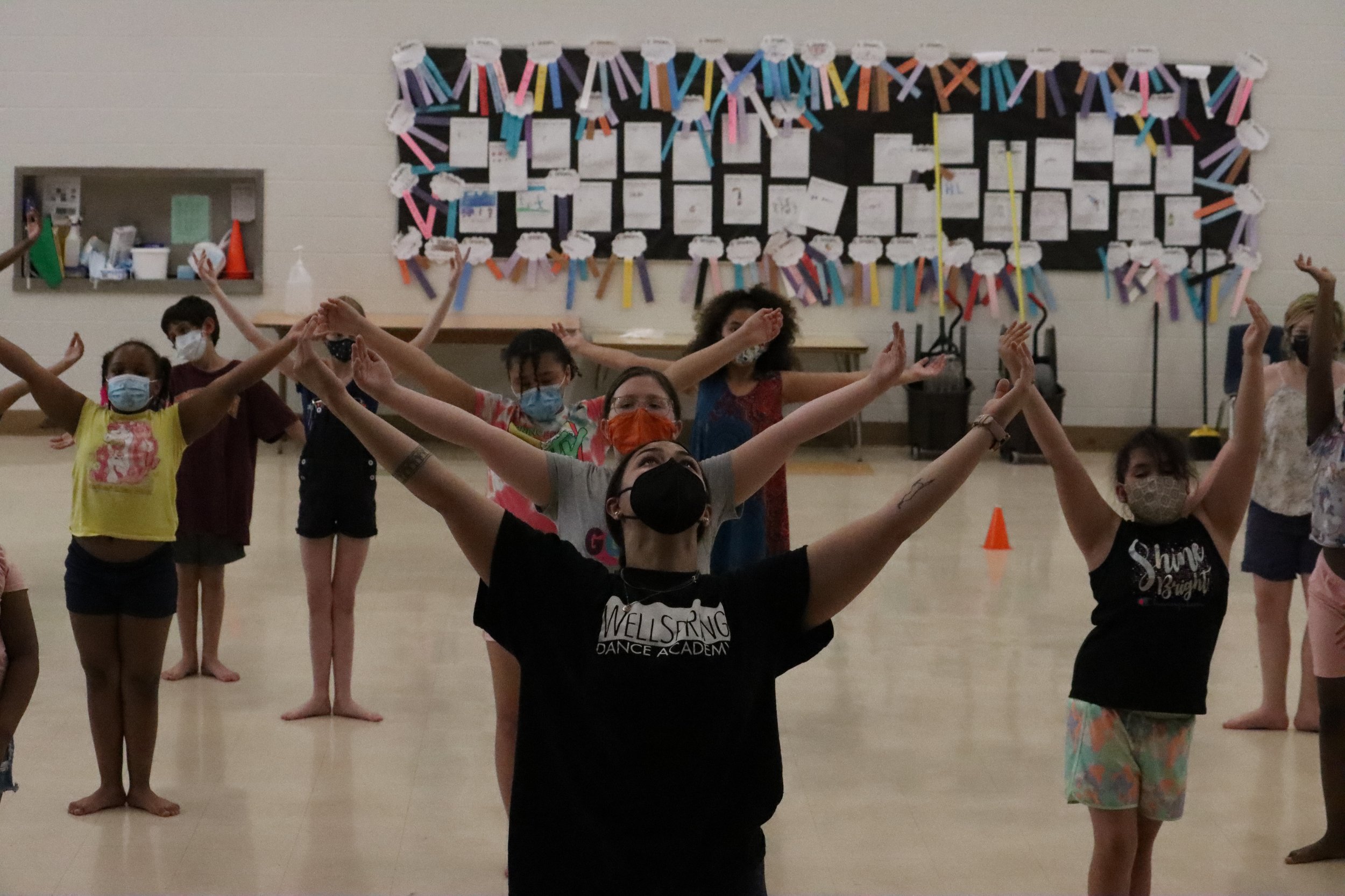 Dance teacher in school with students in arms extended to V 