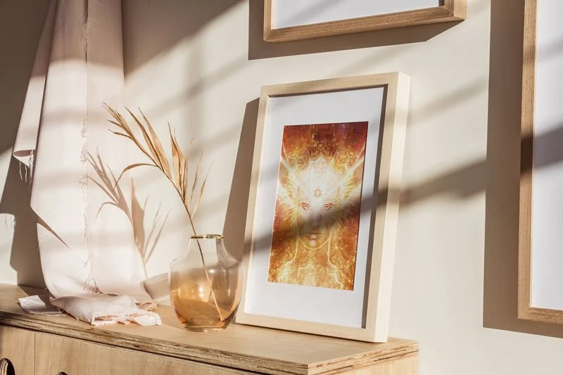 A print of Archangel Metatron is framed and leaning against a wall lit by sunlight.