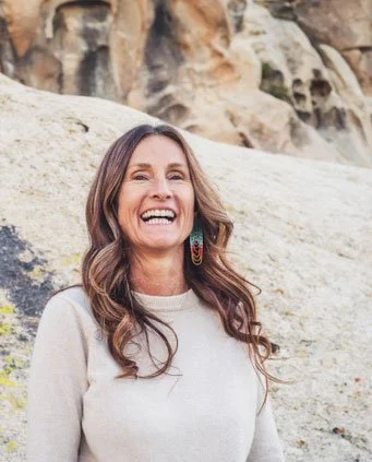 A woman with long brown hair smiling outdoors in front of rock formations