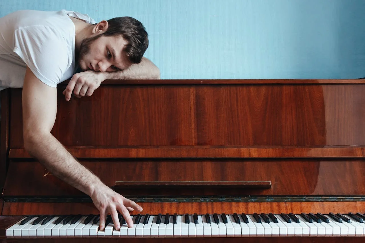 and exhausted adult leans on the piano, tentatively touching the keys.