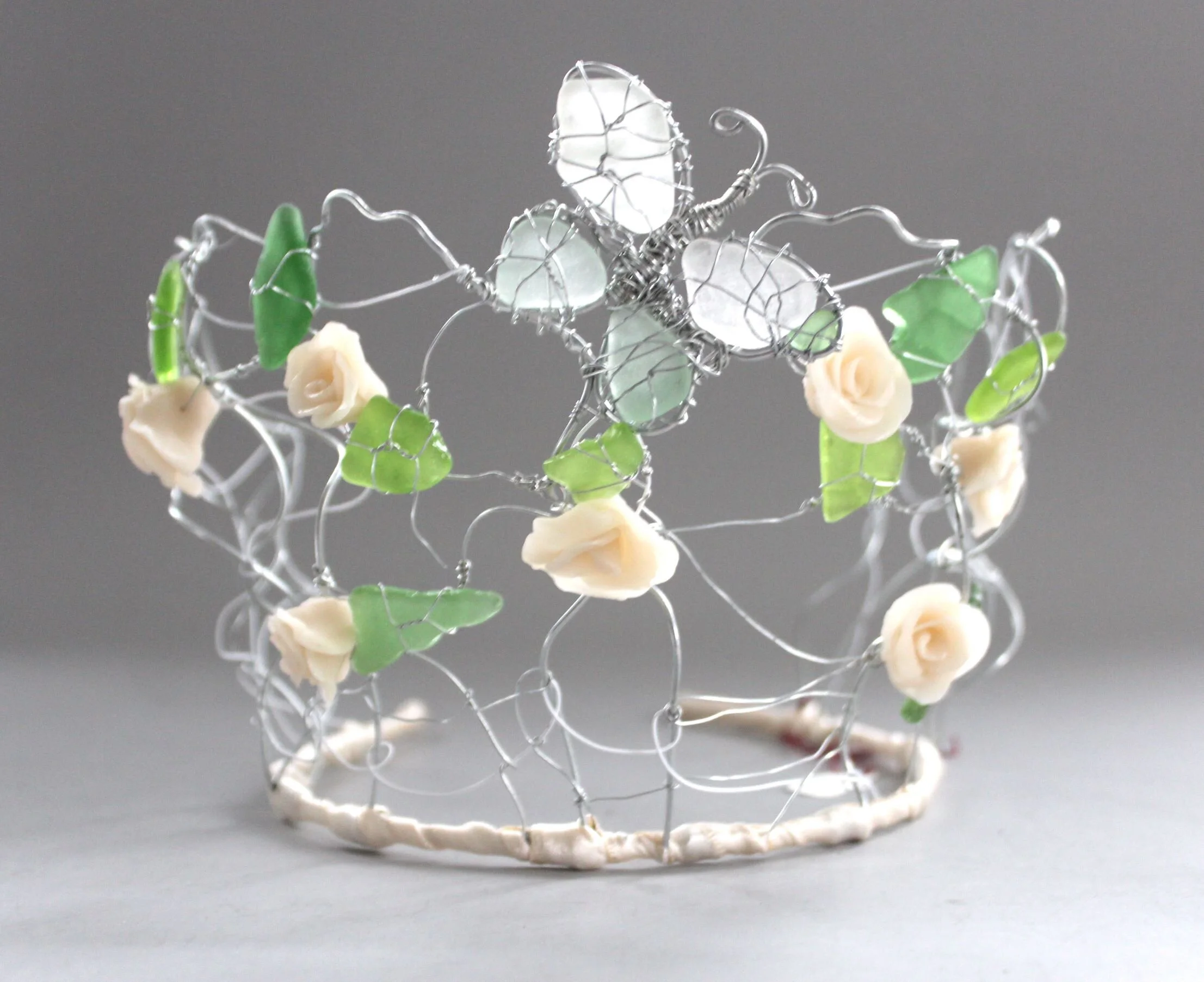 A decorative crown made of silver wire with green and ivory flower-shaped accents.