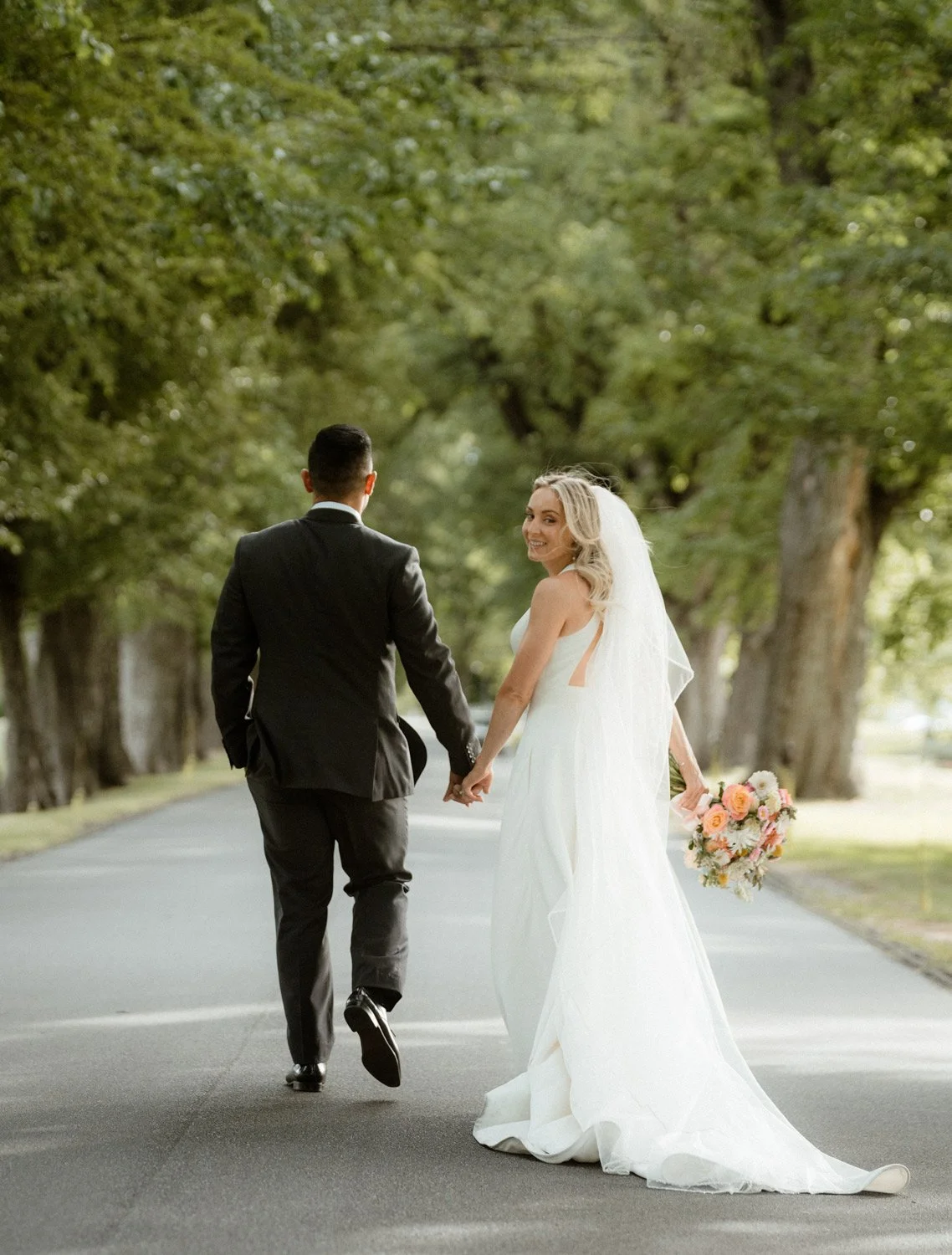 couple walking down Millbrook Resort driveway in Summer, bride with colourful wedding florals