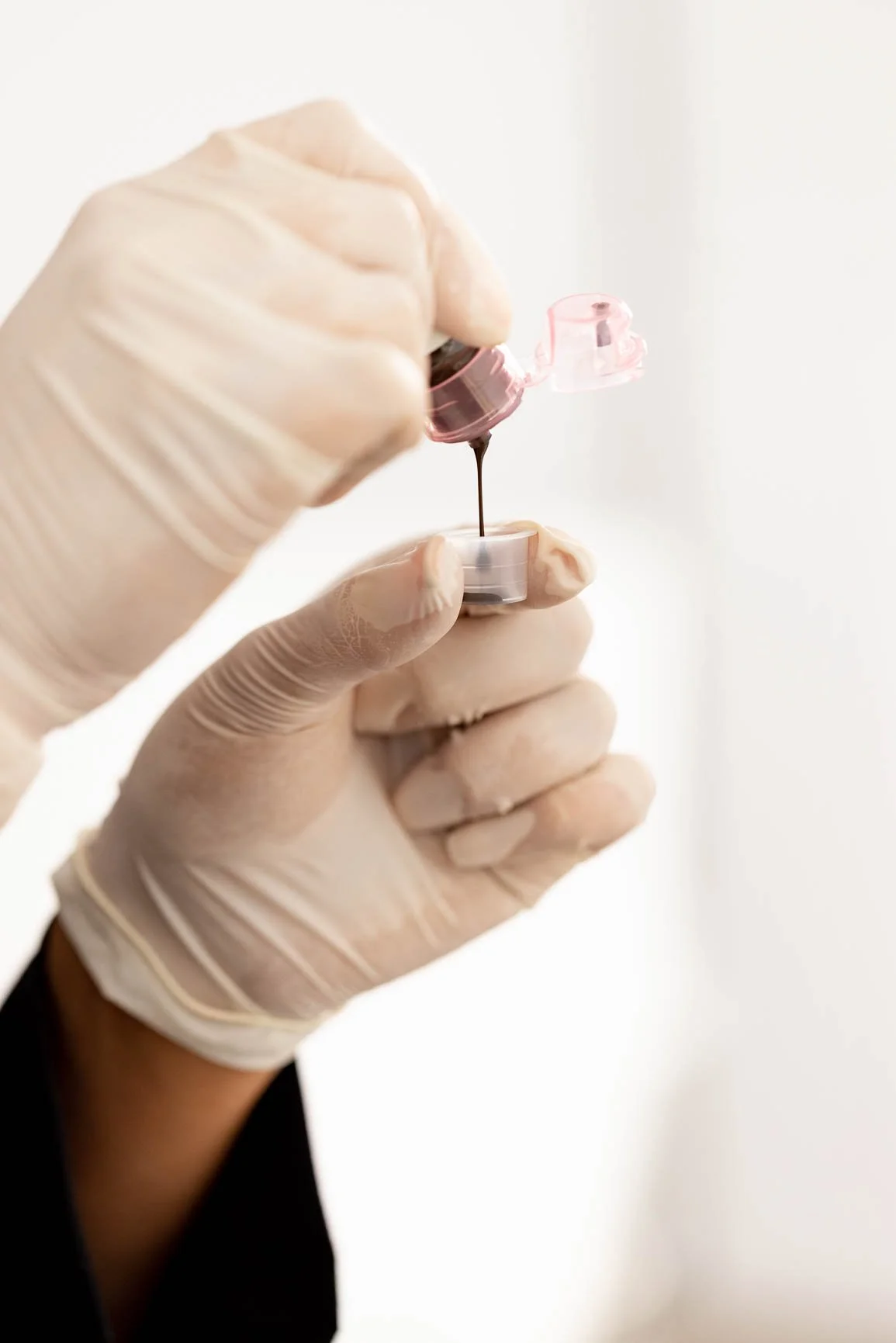 Person wearing gloves holding a small vial with blood being drawn from a medical sample.