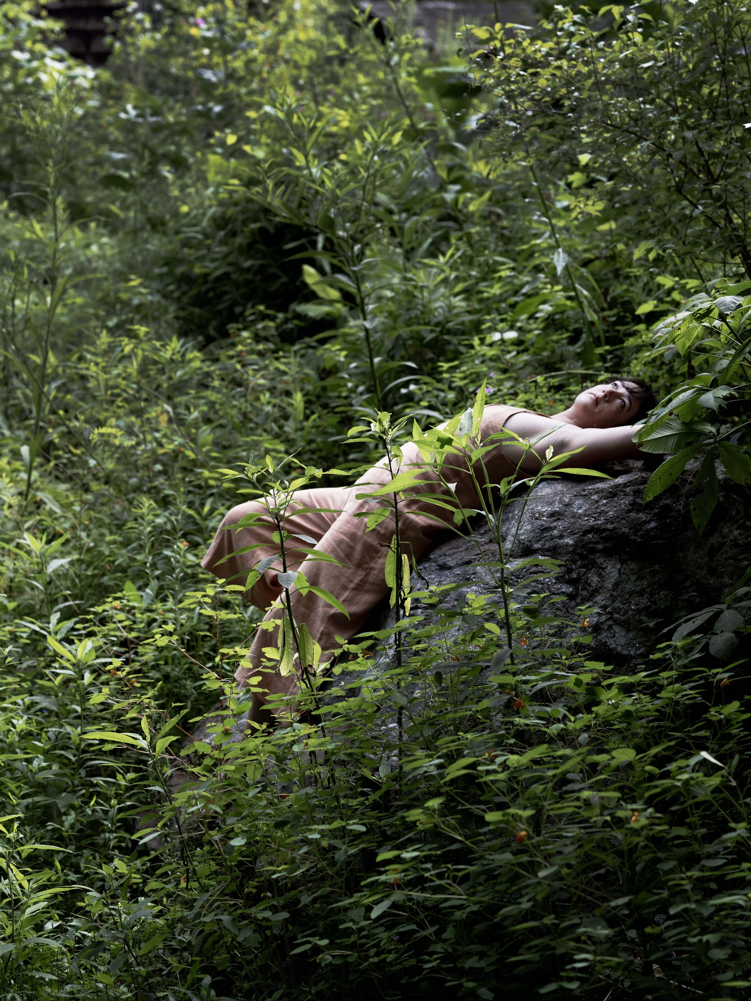 Woman lying on a large rock in a lush green forest with dense vegetation.
