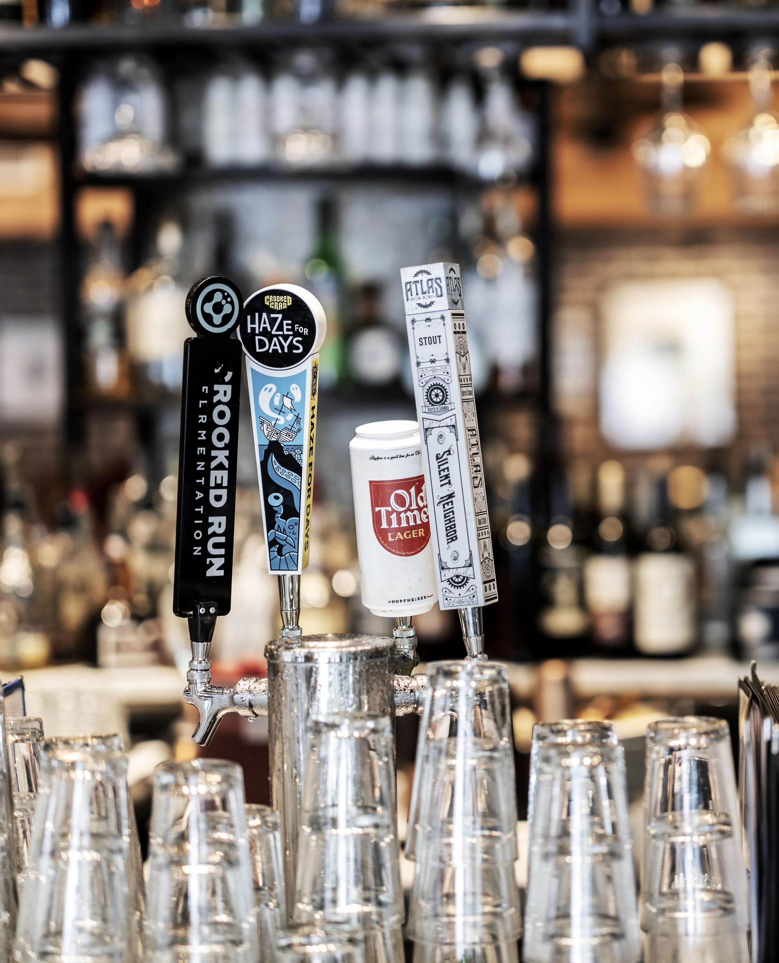Beer taps and several empty beer glasses at a bar, with a background of bottles and bar shelves.