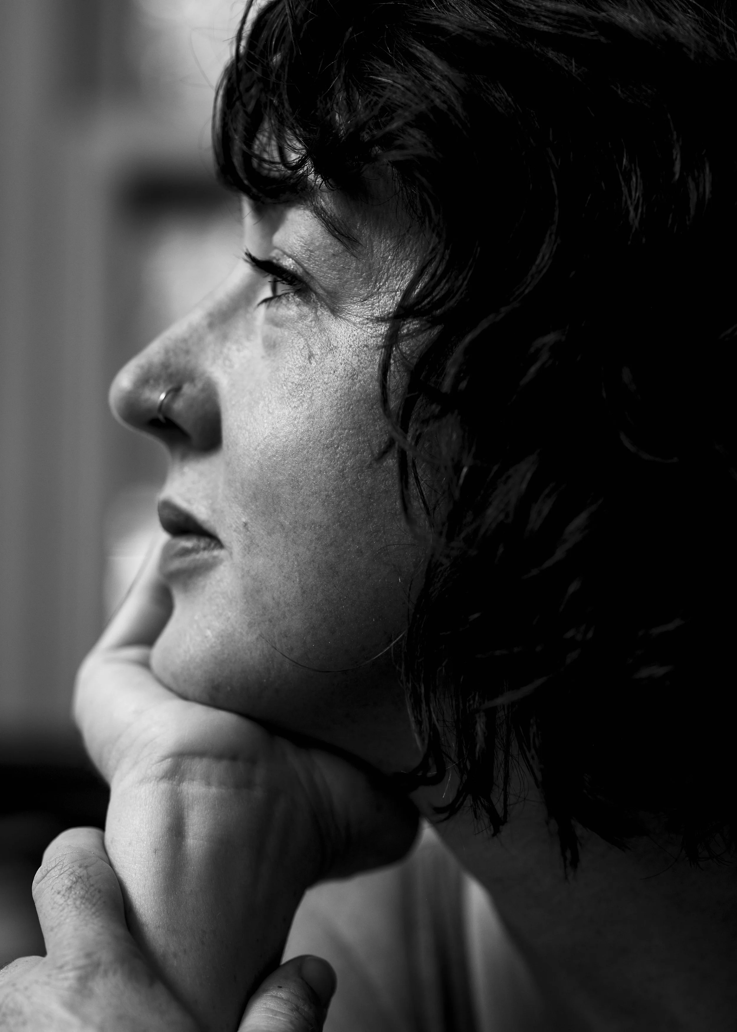 Close-up side profile of a woman with dark curly hair, resting her chin on her hand, in black and white.