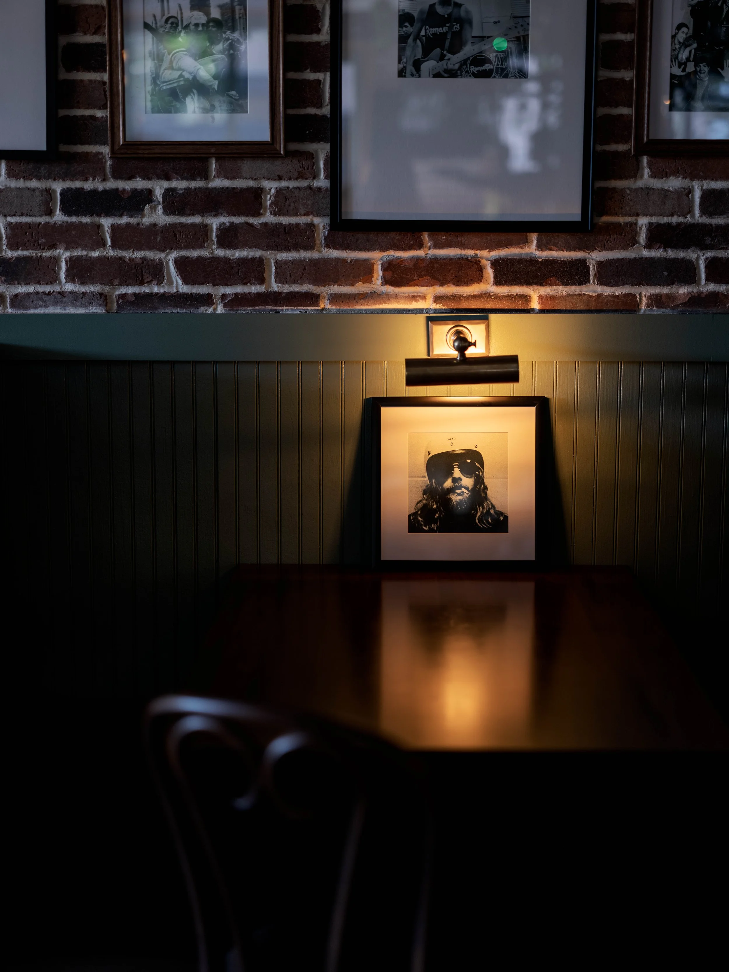 Framed photo of a bearded man with long hair wearing sunglasses and a hat on a dimly lit wall in a cozy, rustic cafe.