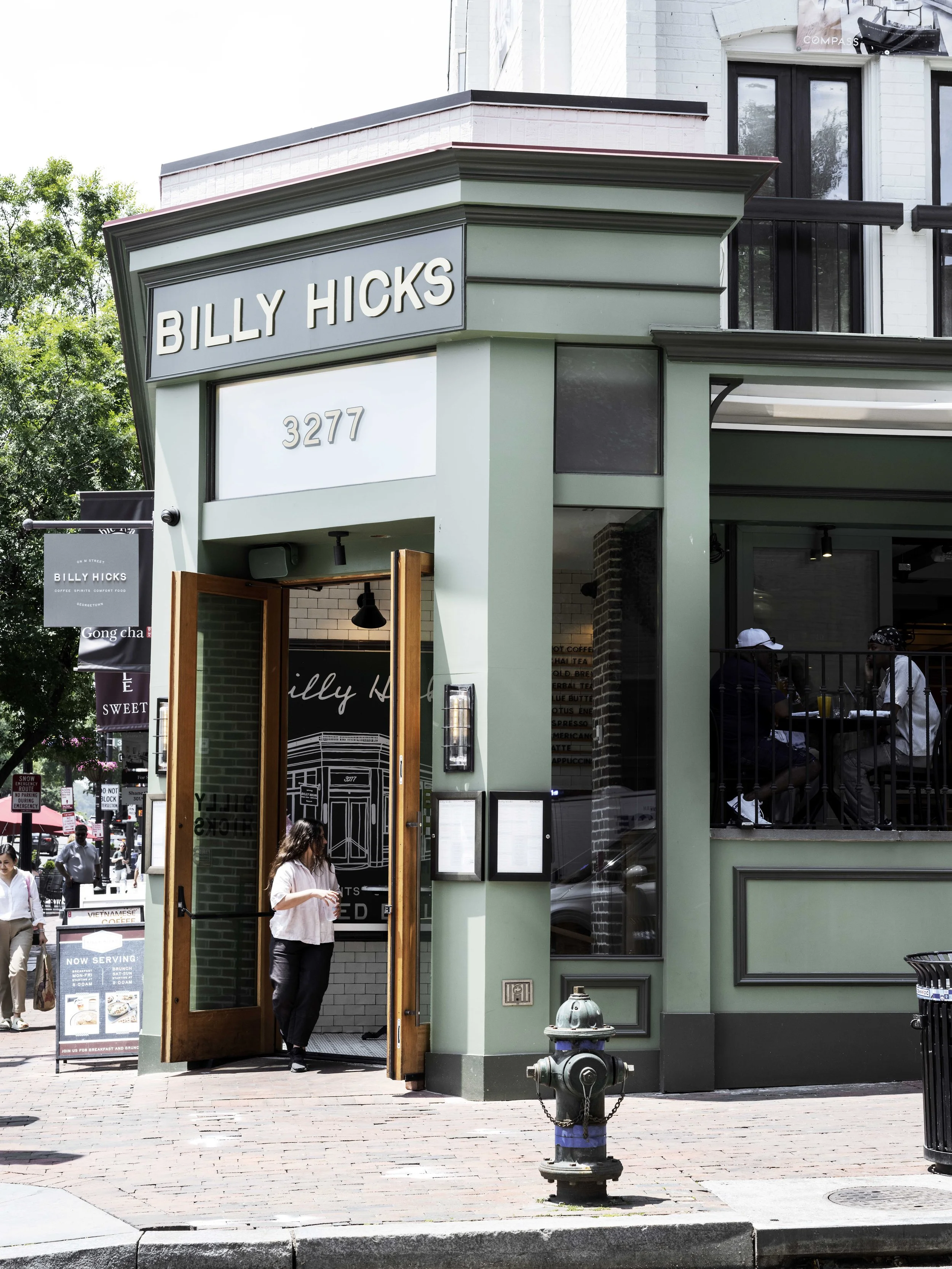 Exterior of Billy Hicks restaurant with open door, a woman standing outside, and a fire hydrant in the sidewalk, in an urban setting.