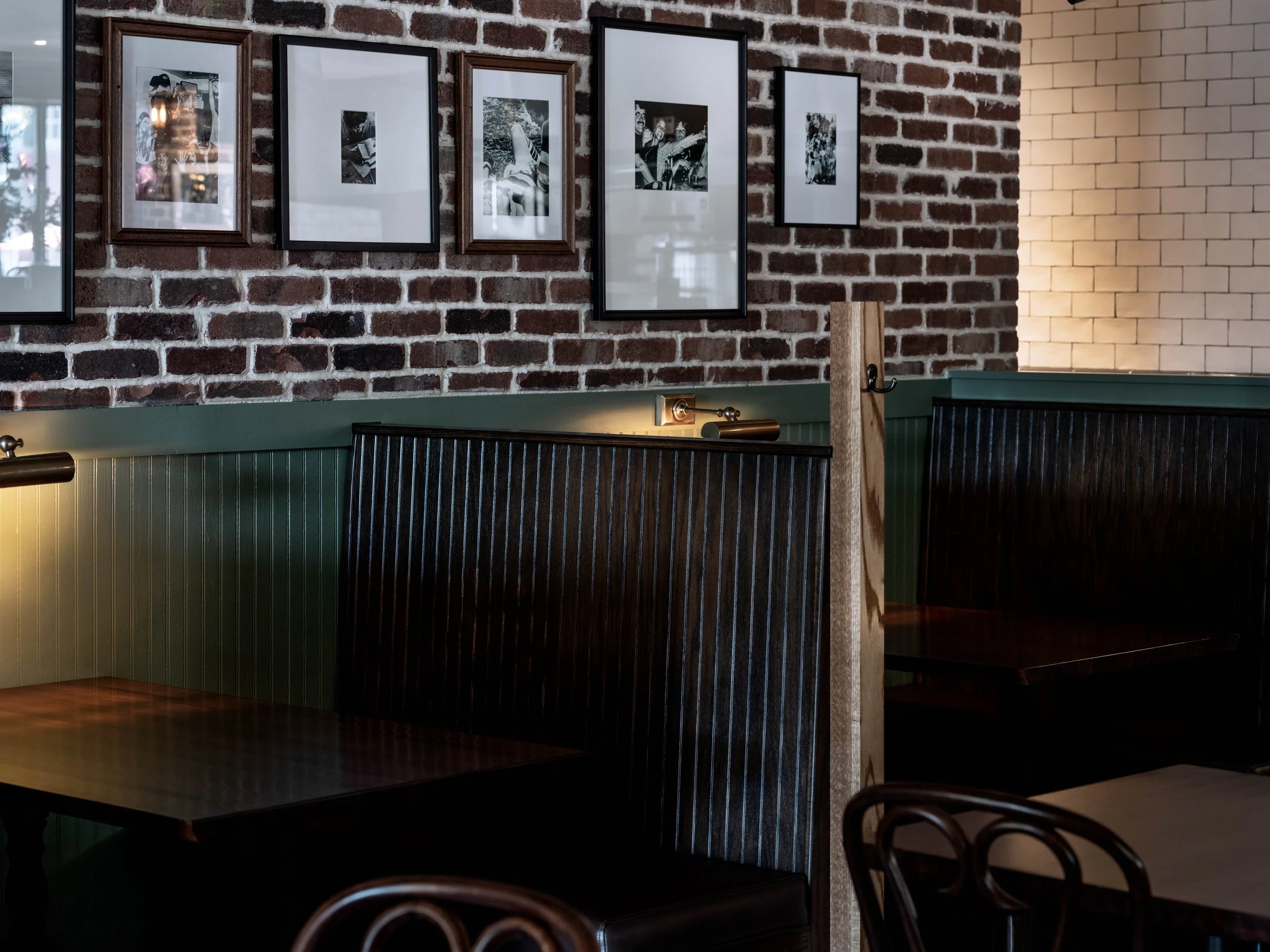 Interior of a restaurant with brick walls, framed black-and-white photos, dark wooden booths, and a green wainscot.