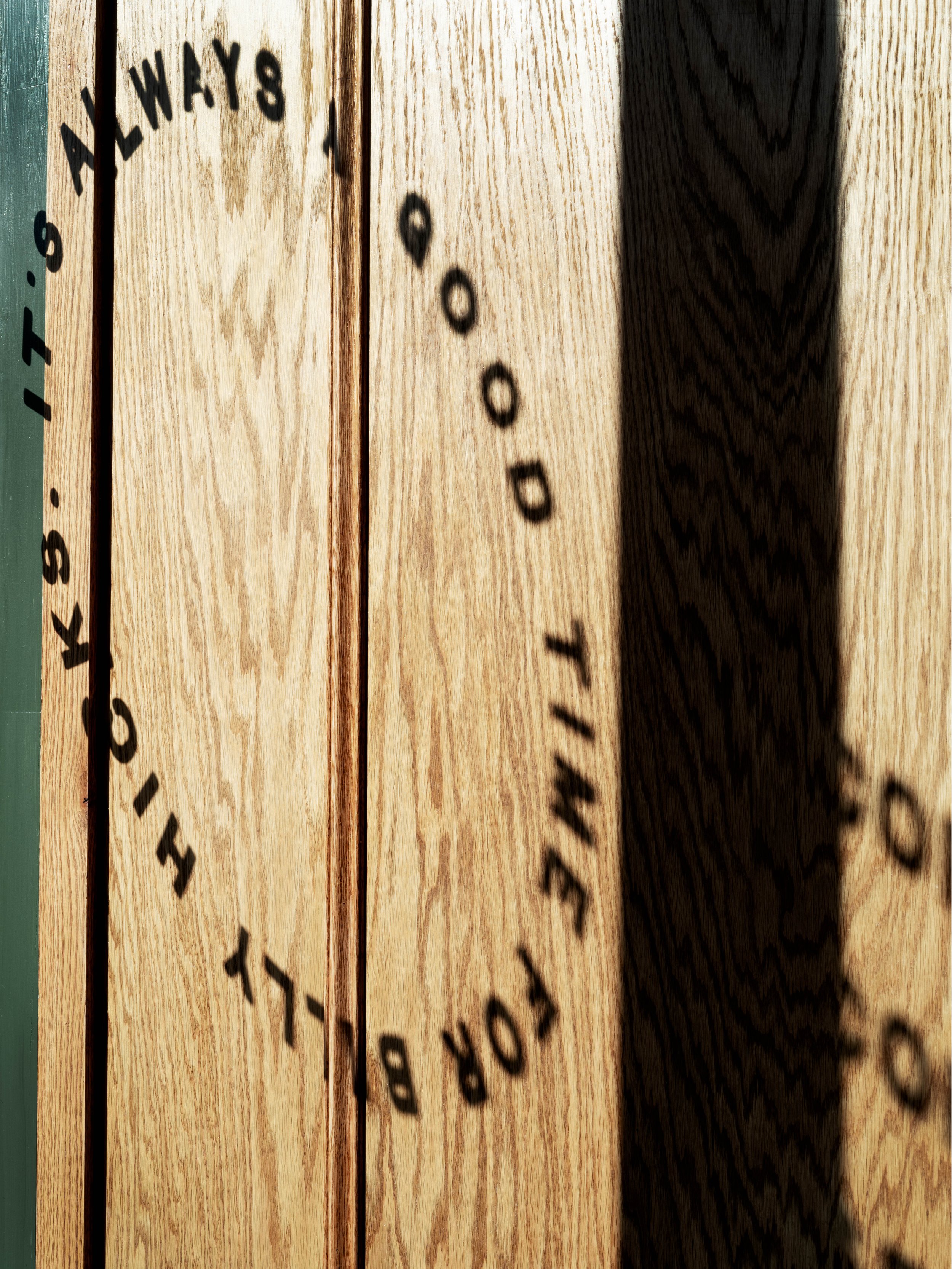 Close-up of a wooden surface with shadowed text that reads "ALL WAYS DOOD" in a circular pattern.