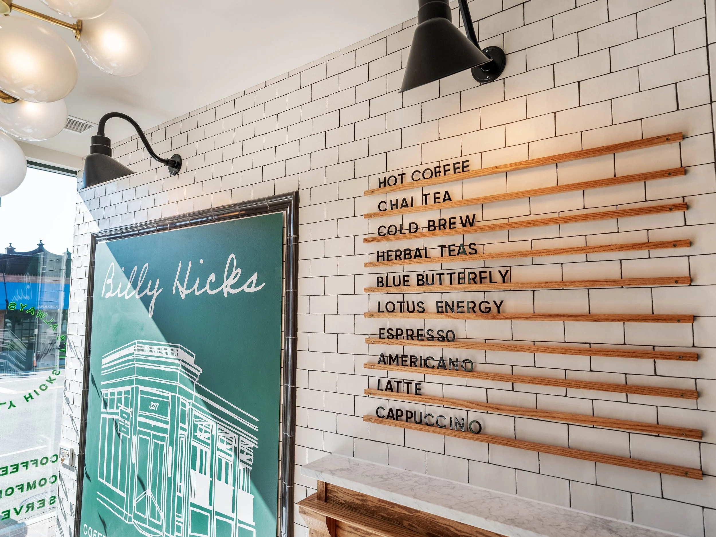 Coffee shop menu on a white brick wall listing beverages such as hot coffee, chai tea, cold brew, herbal teas, blue butterfly, lotus energy, espresso, americano, latte, and cappuccino.