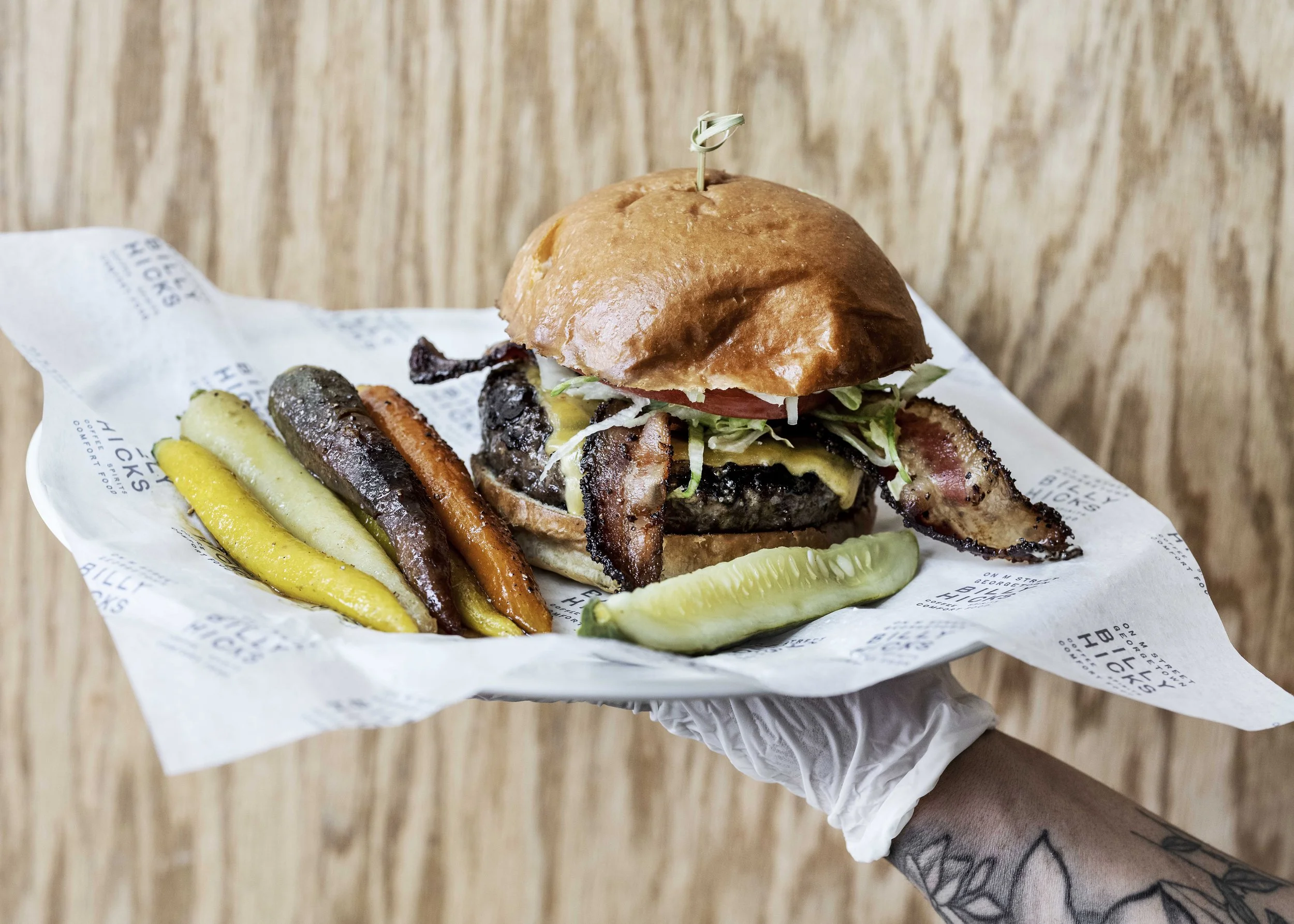 A cheeseburger with lettuce, tomato, bacon, and pickles in a bun, served with assorted pickles.