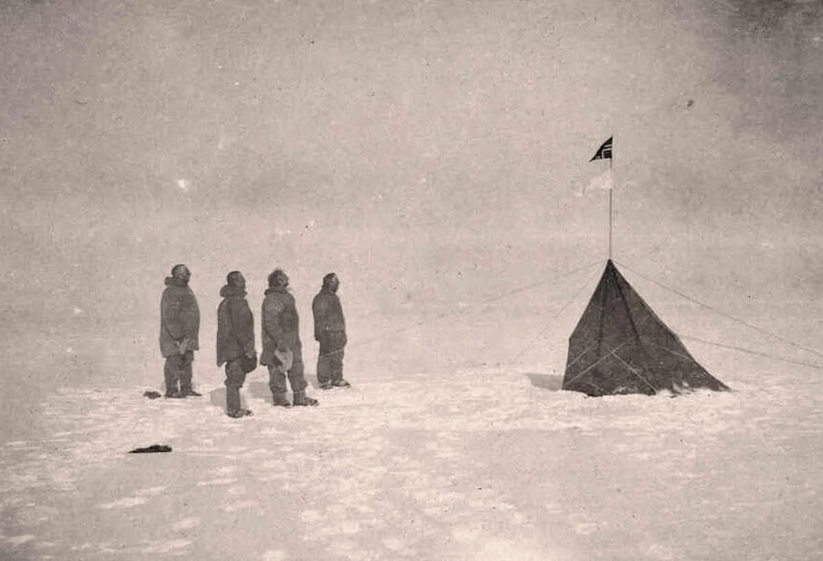 Fire personer i snøen ser på en telt med en flagg på toppen i en isete, snødekt landskap. Roald Amundsen Polar Expedition.