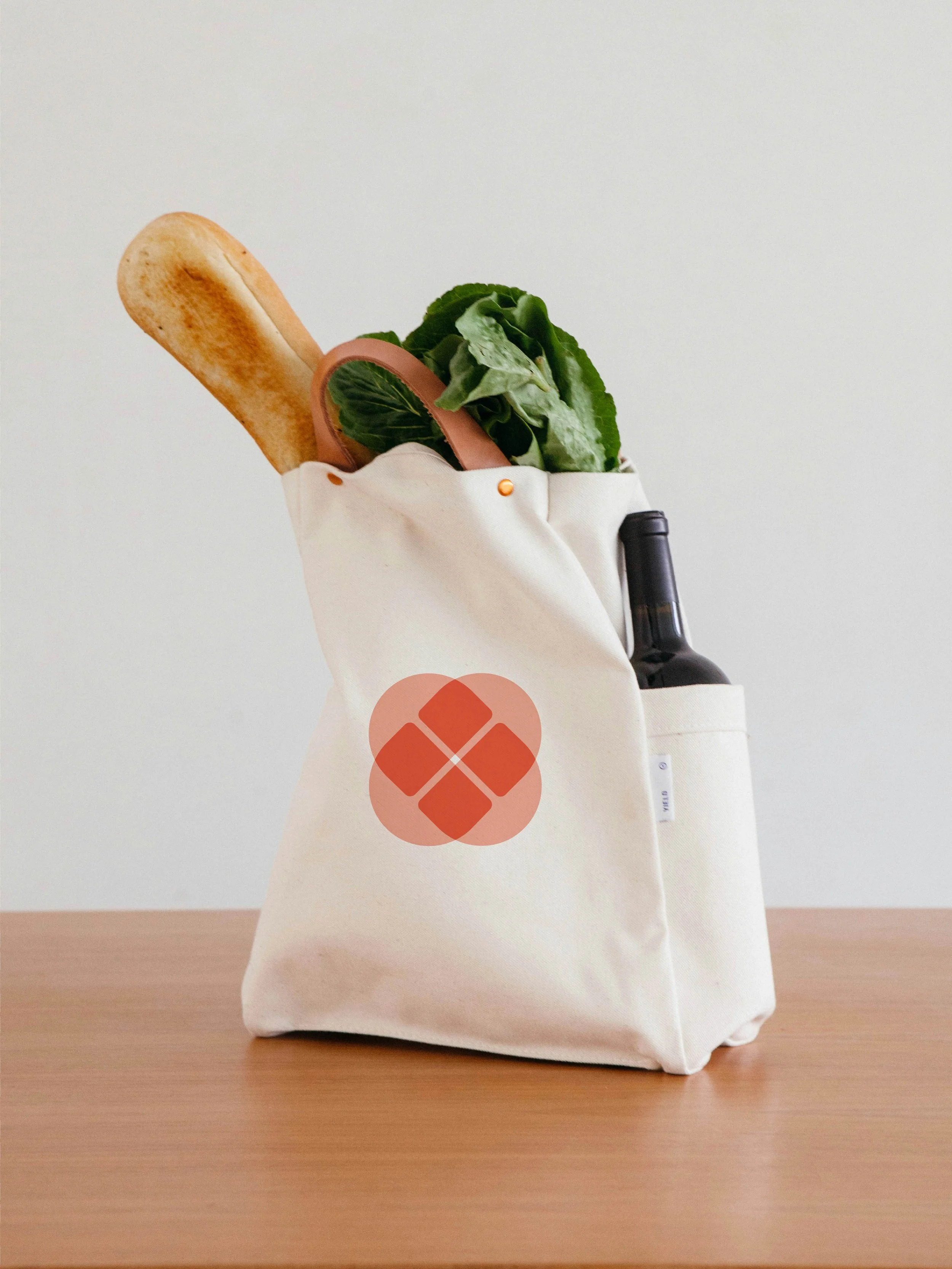 A high quality canvas bag of groceries including bread, lettuce, and a bottle of wine with a pink and red icon on the front representing the brand Gut-Friendly Nutrition.