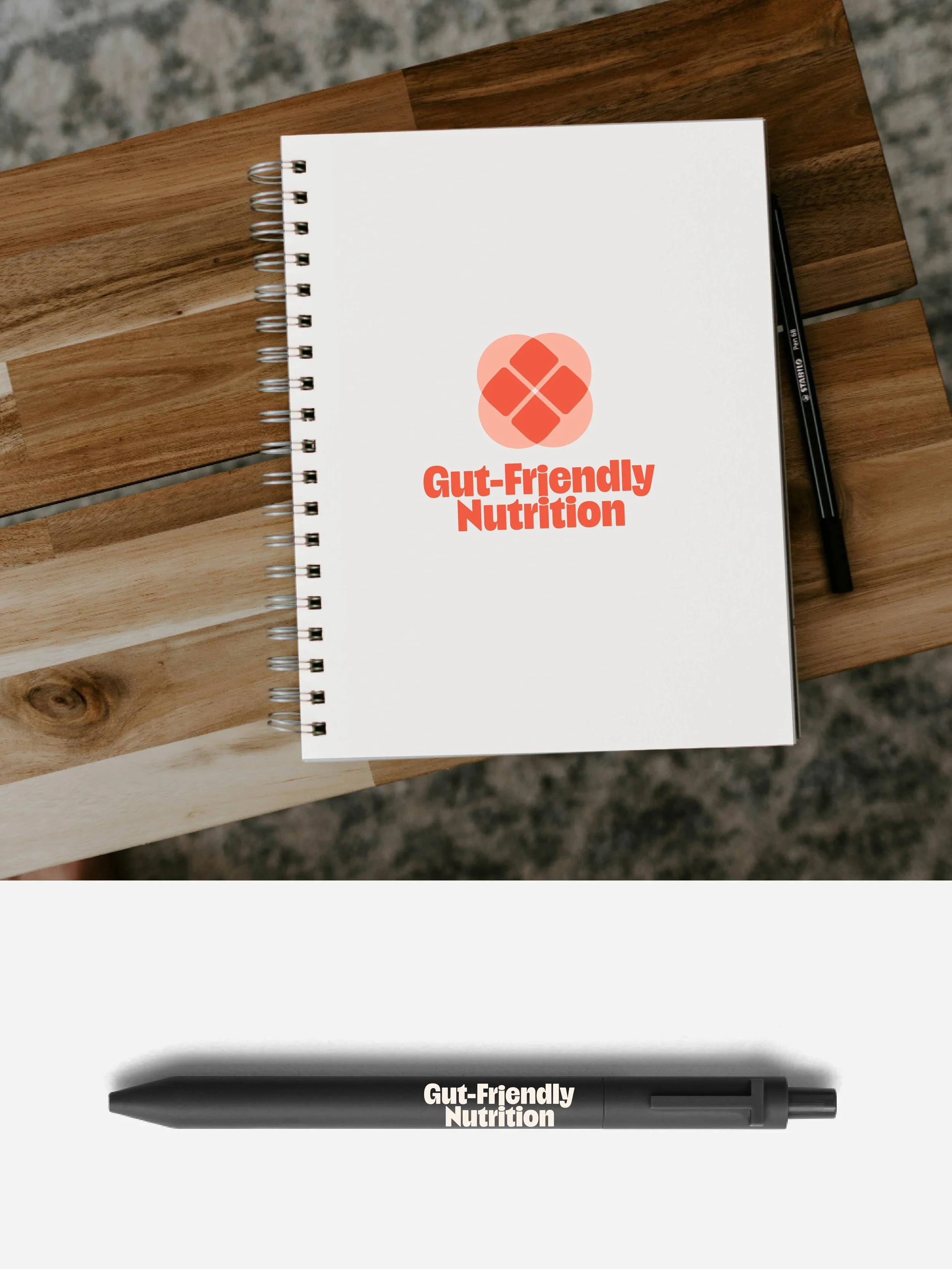 An off-white notebook on a wooden board with the logo for Gut-Friendly Nutrition in pink and red. A pen with the words Gut-Friendly Nutrition.
