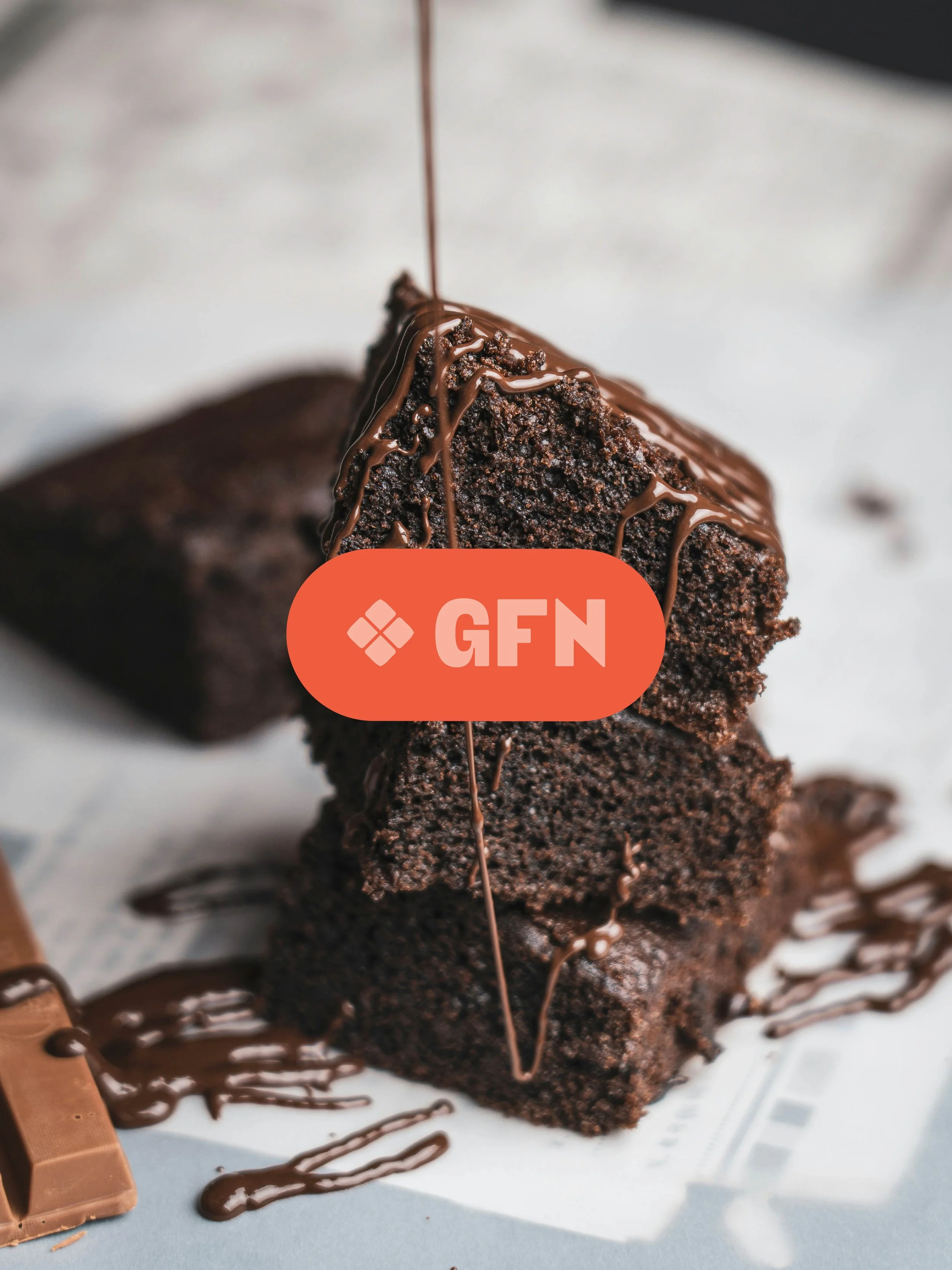 A stack of small brownies being drizzled with chocolate with an overlaid red pill-shape acronym for the brand Gut-Friendly Nutrition.