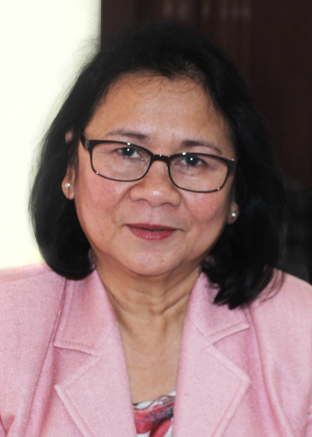 Head and shoulders portrait image of Cecilia looking straight at the camera. She has dark hair in a bob style. She is wearing glasses with black frames, a patterned top, a pink suit jacket and pearl stud earrings.