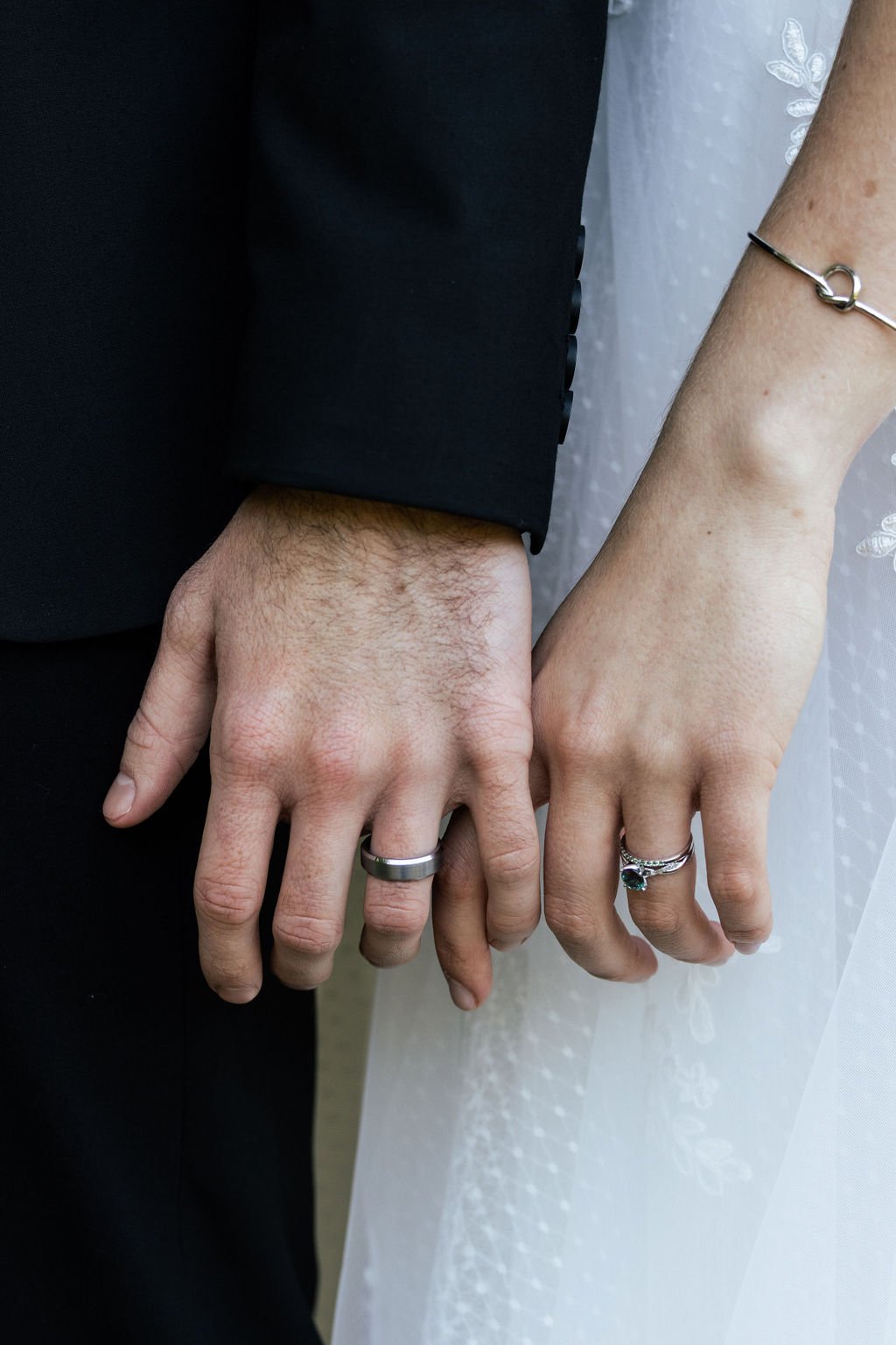 Close-up of a man and woman holding hands, wearing wedding rings, with the man's hand on the left and the woman's hand on the right.