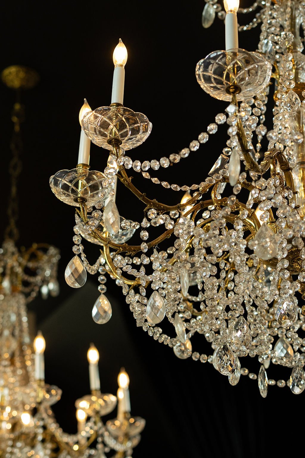 Close-up of a luxurious crystal chandelier with lit candle-shaped bulbs and hanging crystals against a dark background.