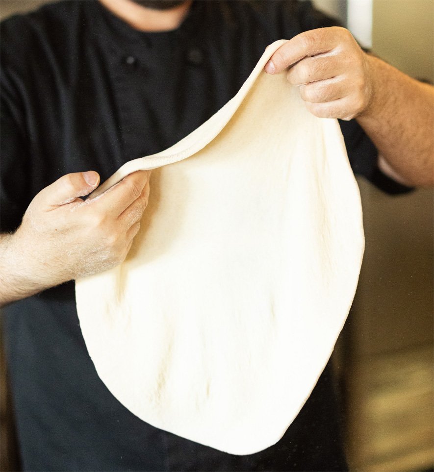 Person stretching and handling a sheet of pizza dough.