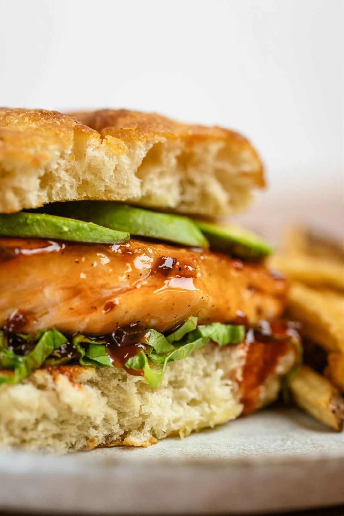 Close-up of a chicken sandwich with pickles, greens, and barbecue sauce on a sandwich bun.
