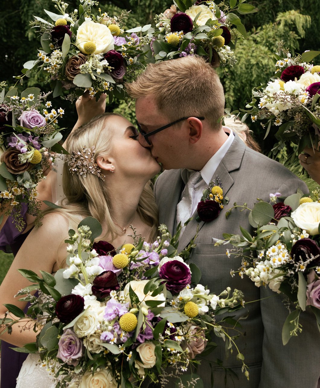 A bride and groom sharing a kiss surrounded by large floral arrangements at their wedding.