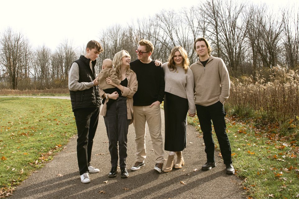 Six people standing together outdoors on a path in a park, smiling and enjoying the day, with leafless trees in the background.
