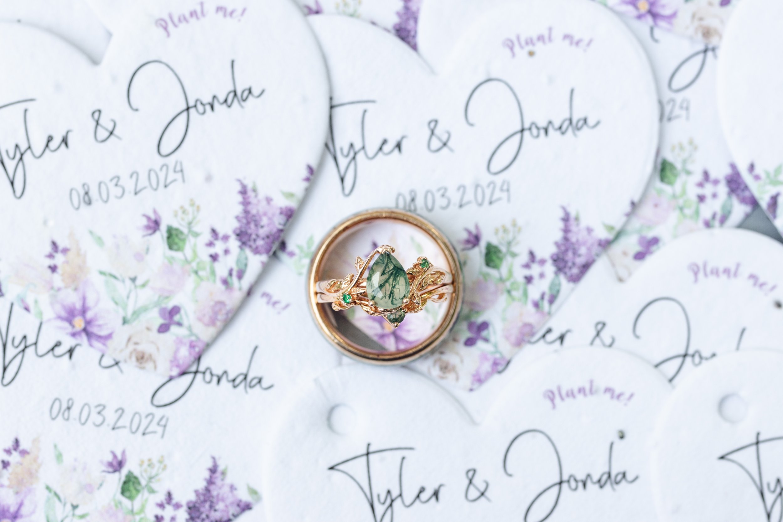 Wedding rings placed on gift tags with floral designs and the text 'Tyler & Jonda', 08.03.2024, and 'Plant me!'