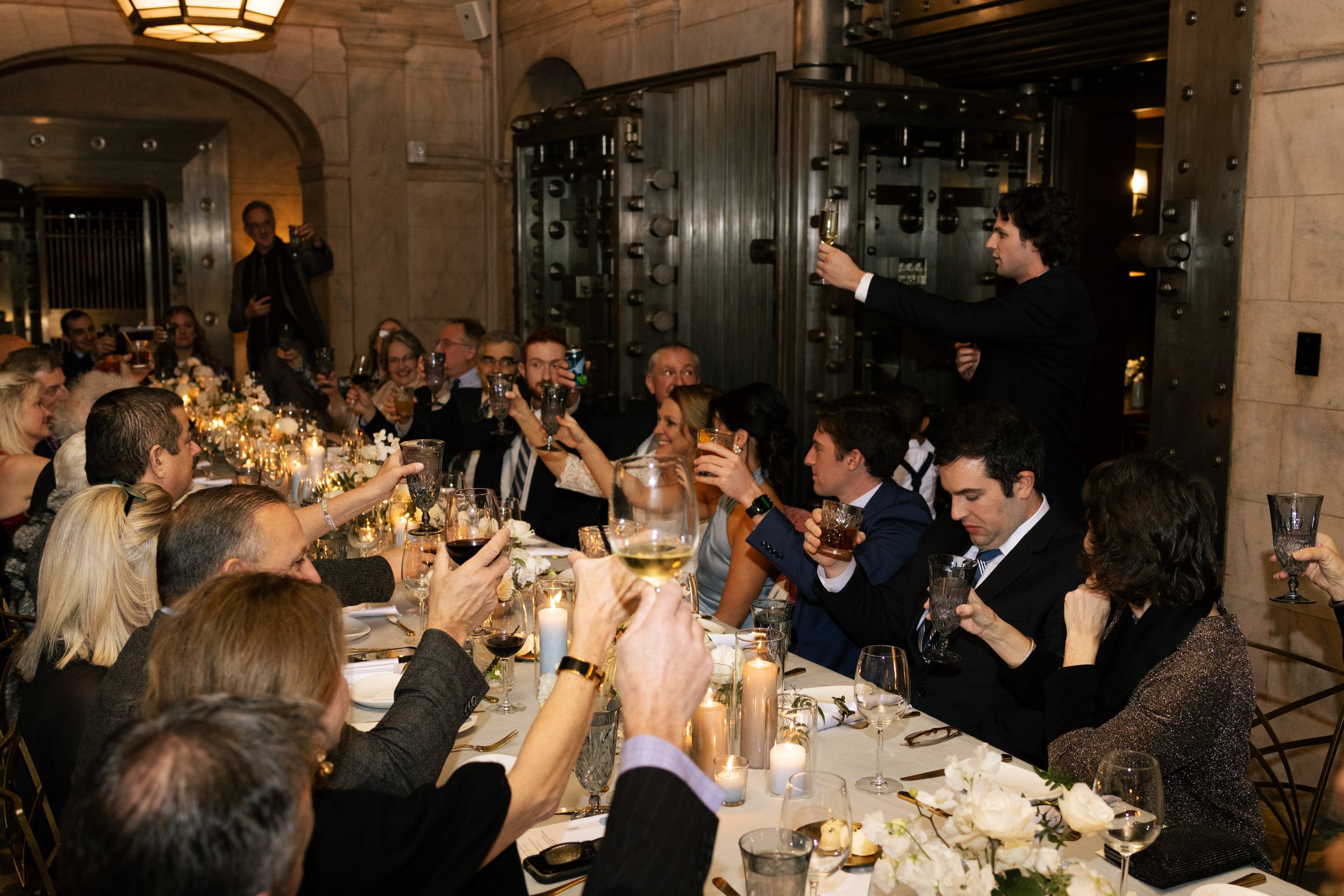 People gathered around a decorated dinner table raising glasses for a toast at a formal celebration in an elegant room.